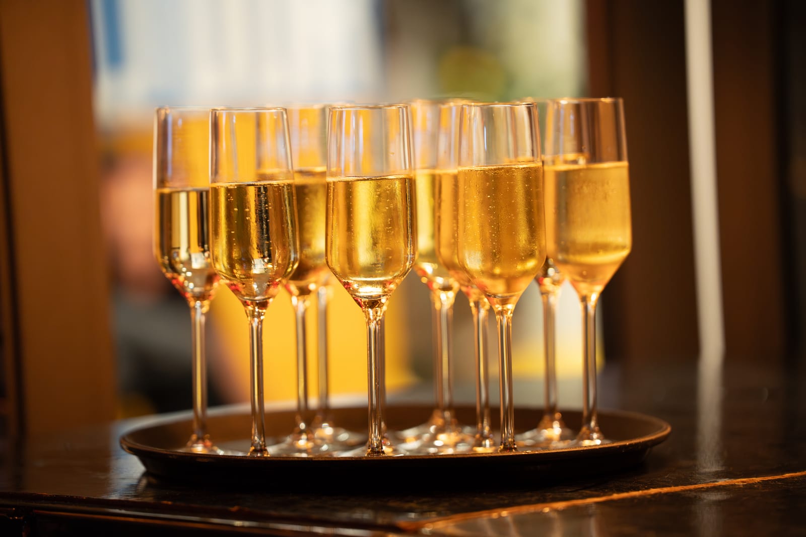 Dienblad vol gevulde champagneflûtes op een donkere houten bar, goudgeel opgelicht door het warme zaallicht